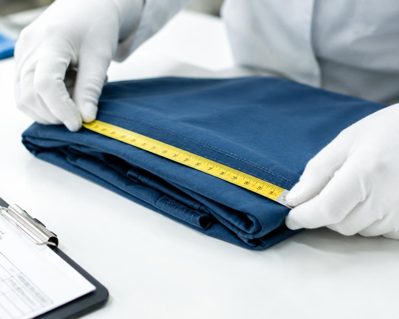 Gloved hands measuring a folded textile product on an inspection table